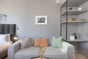 Un salon moderne avec un canapé gris, une œuvre d’art abstraite encadrée et une petite plante posée sur une étagère.