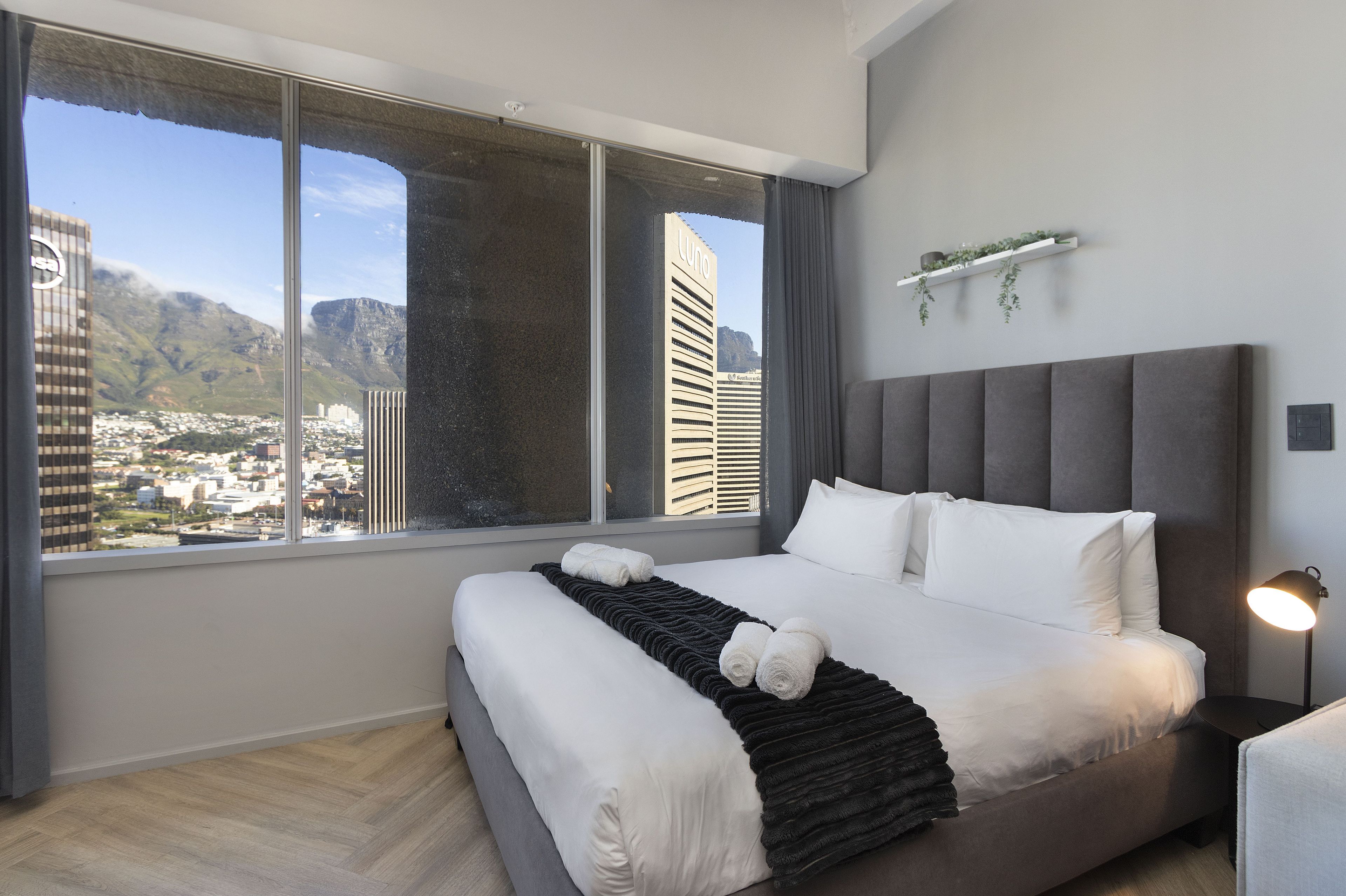 A modern hotel room with a large bed, a view of a cityscape, and a city skyline through the window.