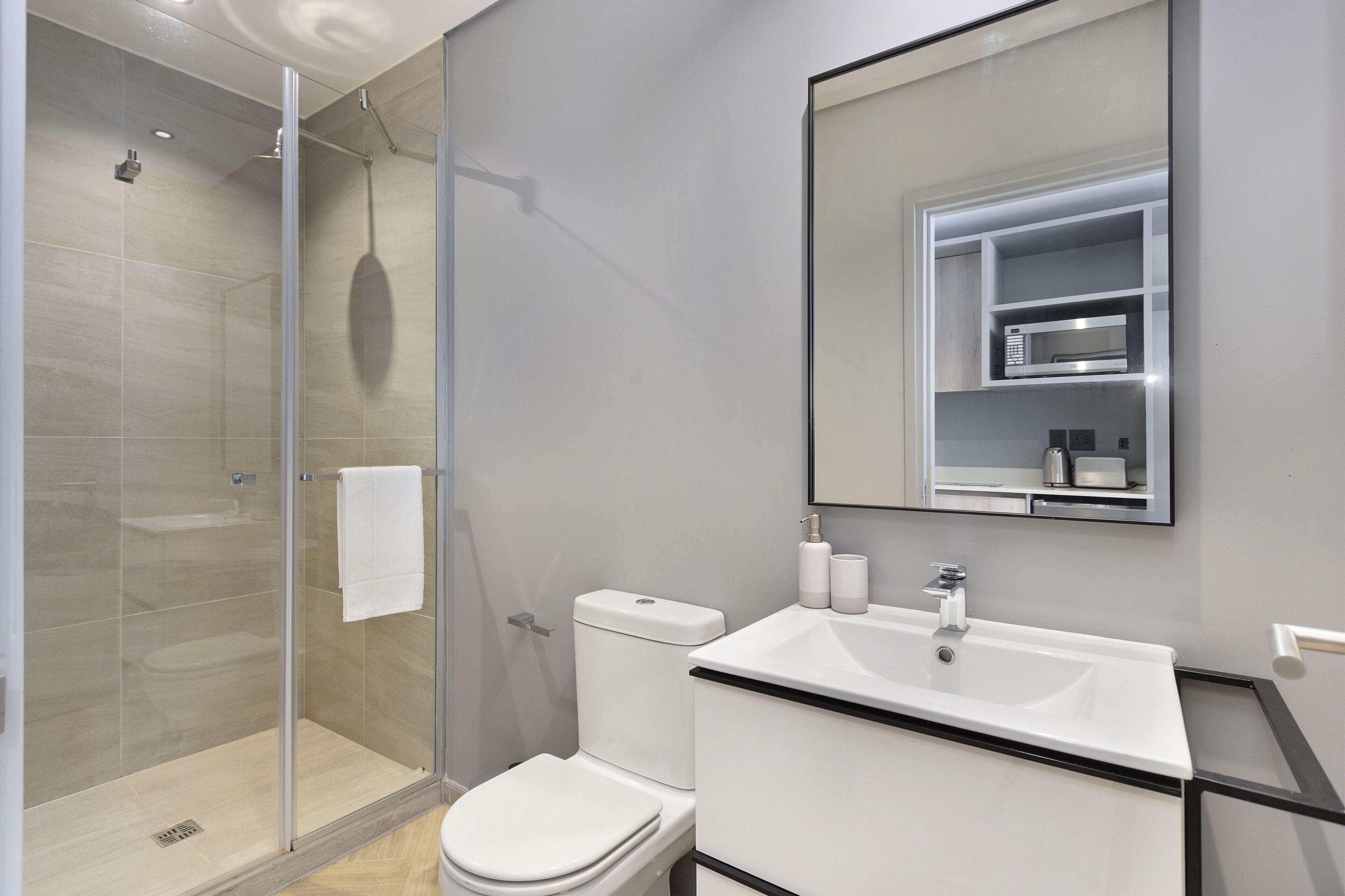 Un baño moderno con ducha envuelta en vidrio, inodoro blanco y lavamanos con espejo superior.