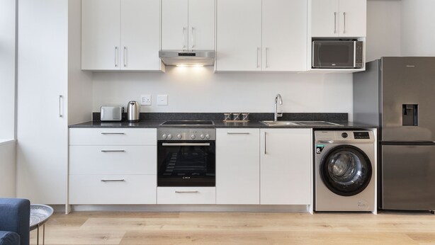 Uma cozinha moderna com armários brancos, forno embutido, micro-ondas, máquina de lavar e frigorífico.