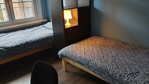 A dormitory room with two single beds, a nightstand with a lamp, a chair, and a window. - Room-room With 2 Separated Beds (Mortsel)