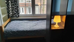 A single bed with a patterned bedspread, a window with a view of buildings, and a lamp in the corner. - Room-room With 2 Separated Beds (Mortsel)