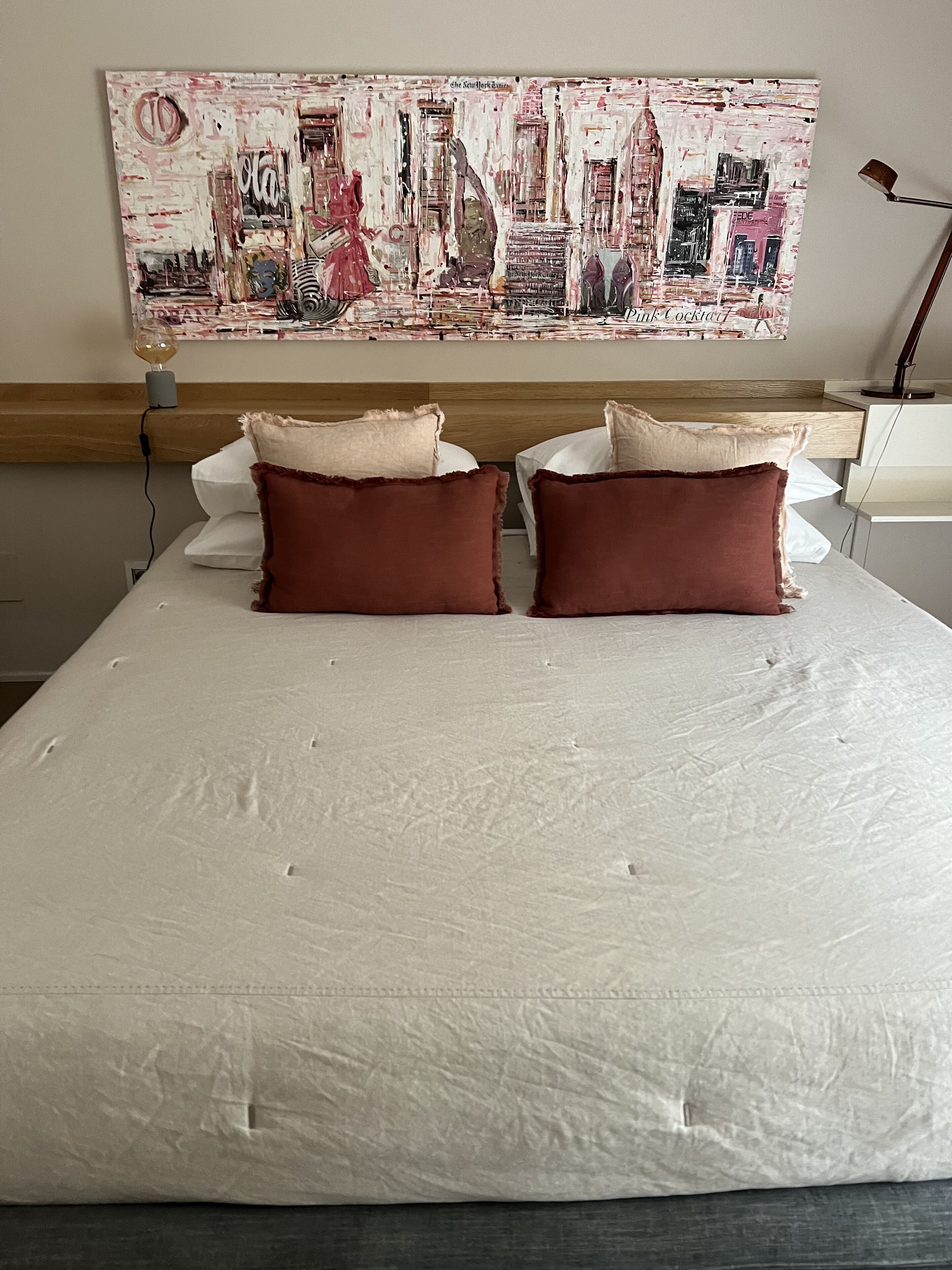A neatly made bed with two pillows and a large abstract painting above it.