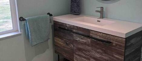 A bathroom with a vanity, a round mirror, a towel rack, and a window.