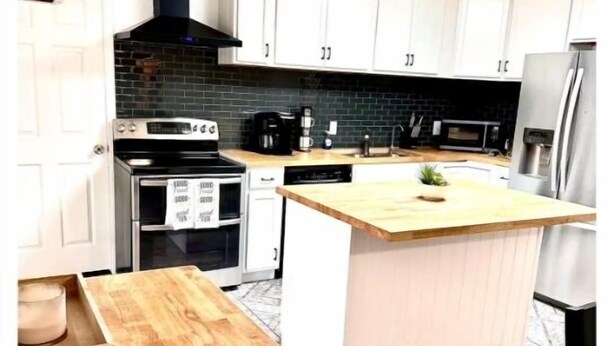 A modern kitchen with white cabinets, a central island, a black stove, and a stainless steel refrigerator.