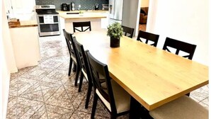 A compact kitchen with white cabinets, a stainless steel refrigerator, and a dining area with a wooden table and chairs.