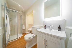 Un baño con cabina de ducha de vidrio, inodoro blanco, lavamanos con dos botellas de jabón y espejo sobre el lavamanos.