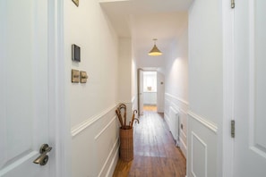 A narrow hallway with white walls, a wooden floor, a basket with walking sticks, and a door with a brass handle. - Dreamy Town House Apartment in Dunkeld (Dunkeld)
