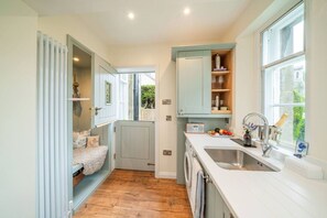 A compact kitchen with a built-in washing machine, a sink with a window view, and a small seating area with a door leading to a garden.