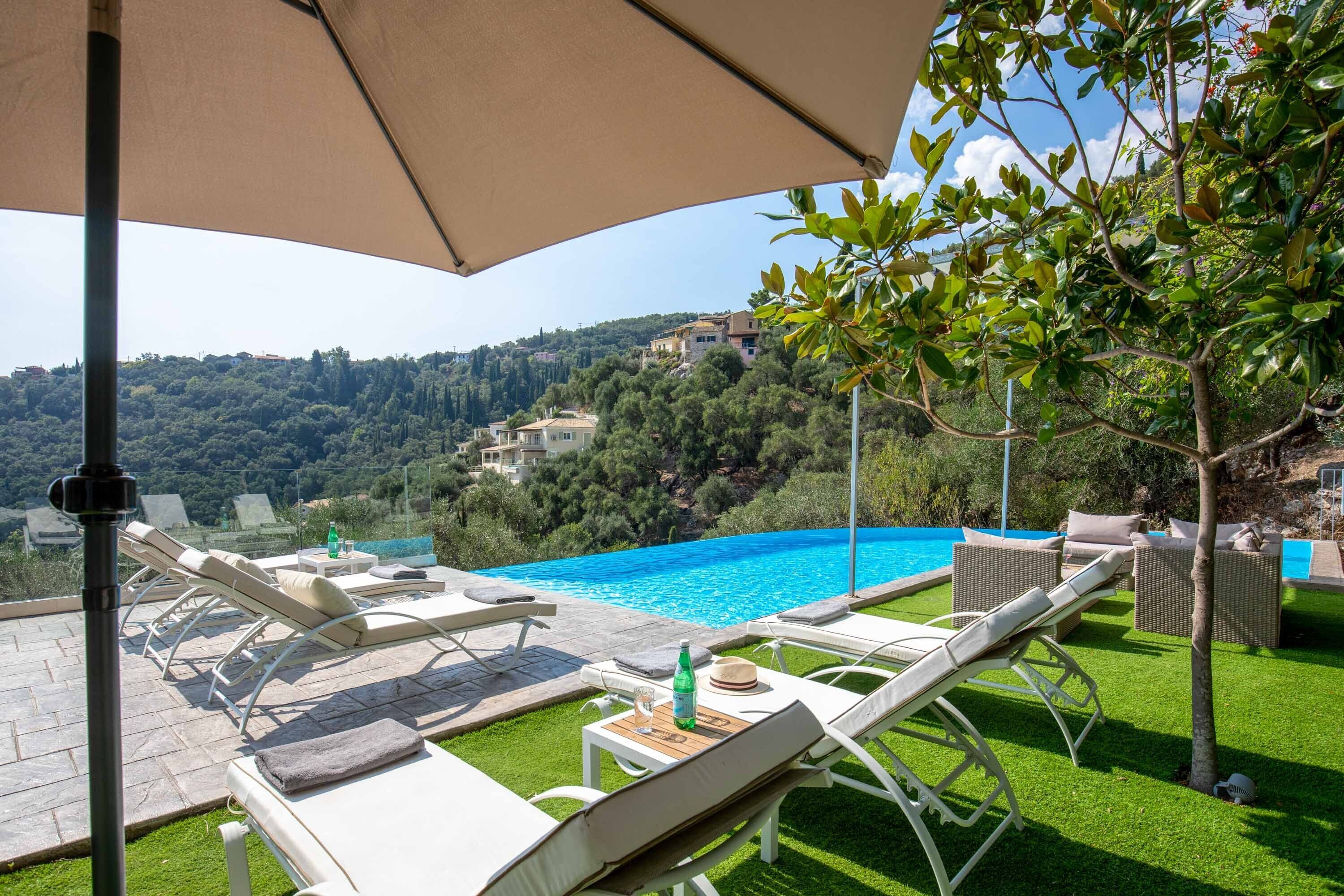 Ein Poolbereich mit Liegestühlen, einem Tisch mit Flasche und Glas sowie Blick auf eine Hügelkuppe mit Gebäuden.
