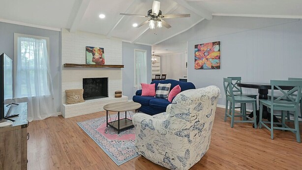 Ein Wohnzimmer mit Kamin, einem blauen Sofa, einem gemusterten Sessel, einem Esstisch mit Stühlen und Kunstwerken an den Wänden.