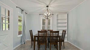 Ein Esszimmer mit Holztisch und Stühlen, einer Kristallleuchter und einem Fenster mit Vorhängen.