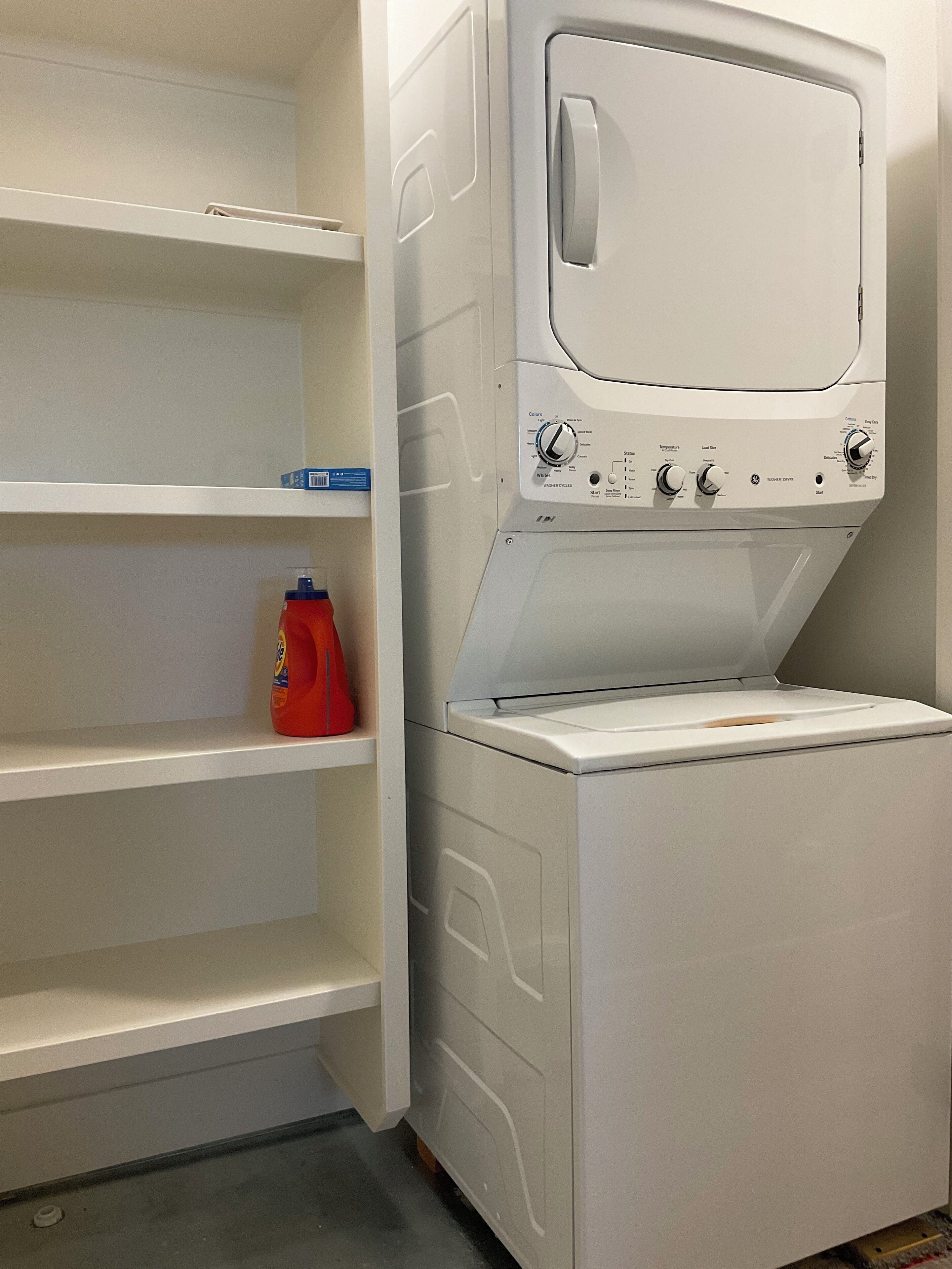Une buanderie équipée d’un lave-linge et d’un sèche-linge, d’étagères pour ranger la lessive et d’un drain au sol.