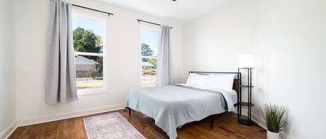 Un dormitorio con cama, lámpara de pie, ventilador de techo y ventana con cortinas.