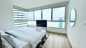 A modern bedroom with a bed, a flat-screen TV, large windows, and a view of a cityscape. - Santa Ana Guayaquil Lux Coliving Ecuador (Guayaquil)