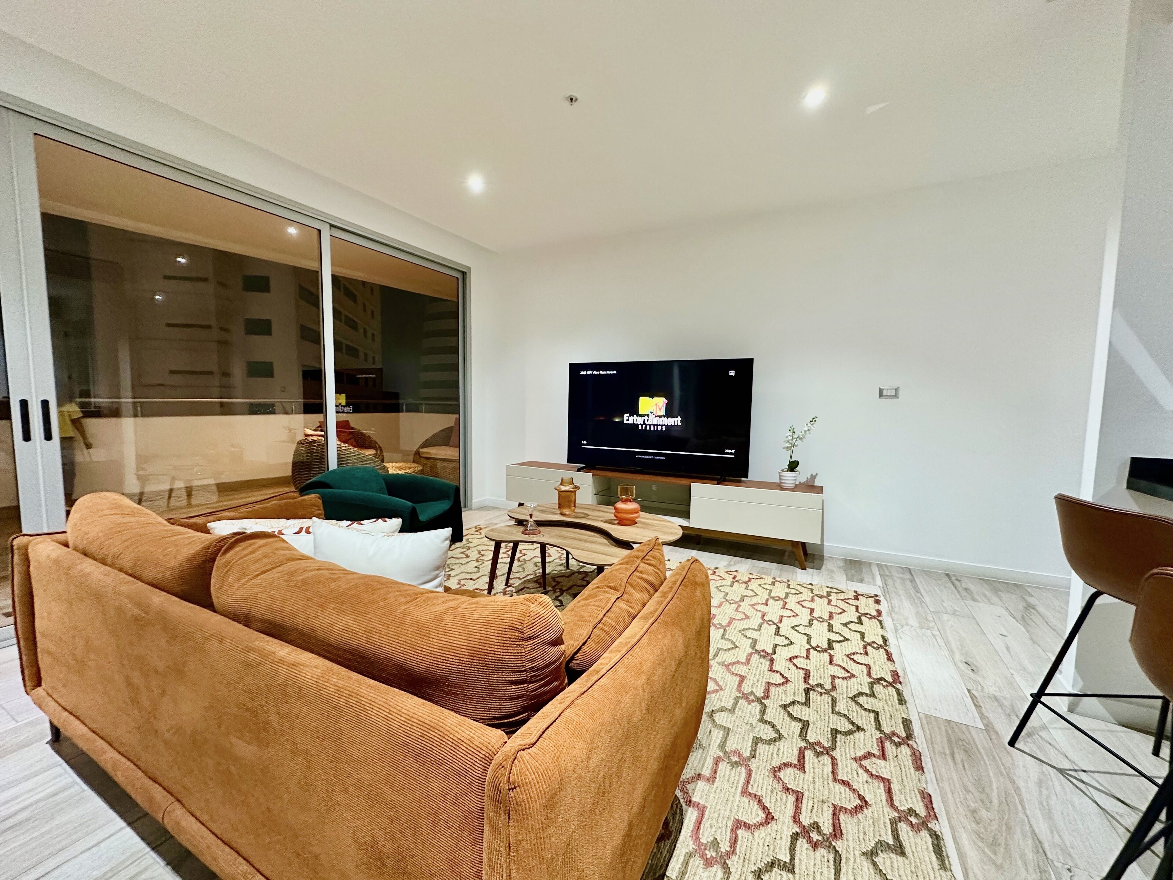 A modern living room with a large TV, a sofa, a coffee table, and a patterned rug.