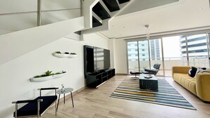 A modern living room with a staircase, a flat-screen TV, a sofa, and a coffee table. - Santa Ana Guayaquil Lux Coliving Ecuador (Guayaquil)