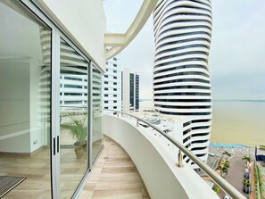 Un edificio moderno con un balcón curvo que da a una playa y otros rascacielos.