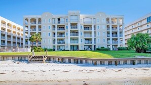 Ein Strandhotel mit mehreren Balkonen, einer Rasenfläche und einem Sandstrand.