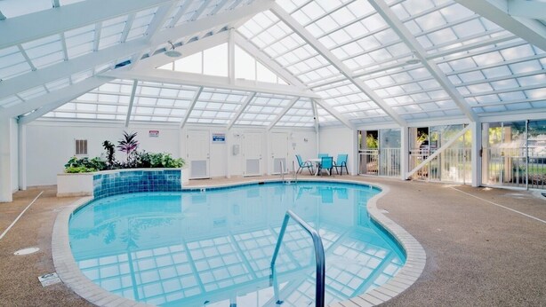 Ein Innenpool mit Glasdach, umgeben von einer gefliesten Terrasse und einigen Stühlen.