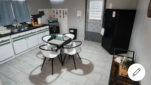 A compact kitchen with white cabinets, a black refrigerator, a dining table with chairs, and a hanging light fixture. - La Posita Beach House  (Cabo Rojo)