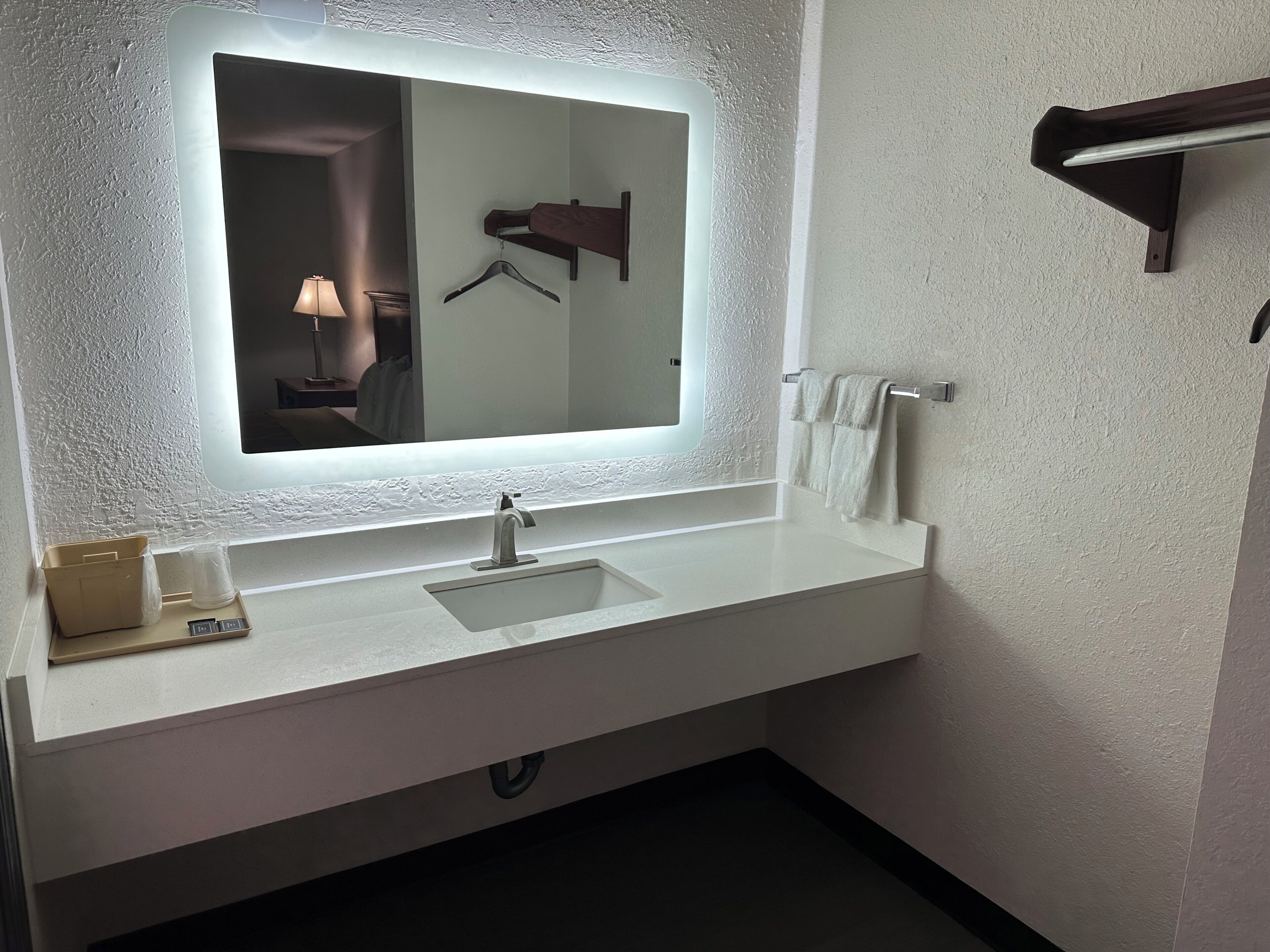 A bathroom with a large mirror, a white sink, a towel rack, and a hanging towel.