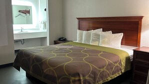 Ein Hotelzimmer mit einem Bett, einem Nachttisch, einer Kommode, einem Spiegel und einem Badezimmer mit Handtuchhalter.