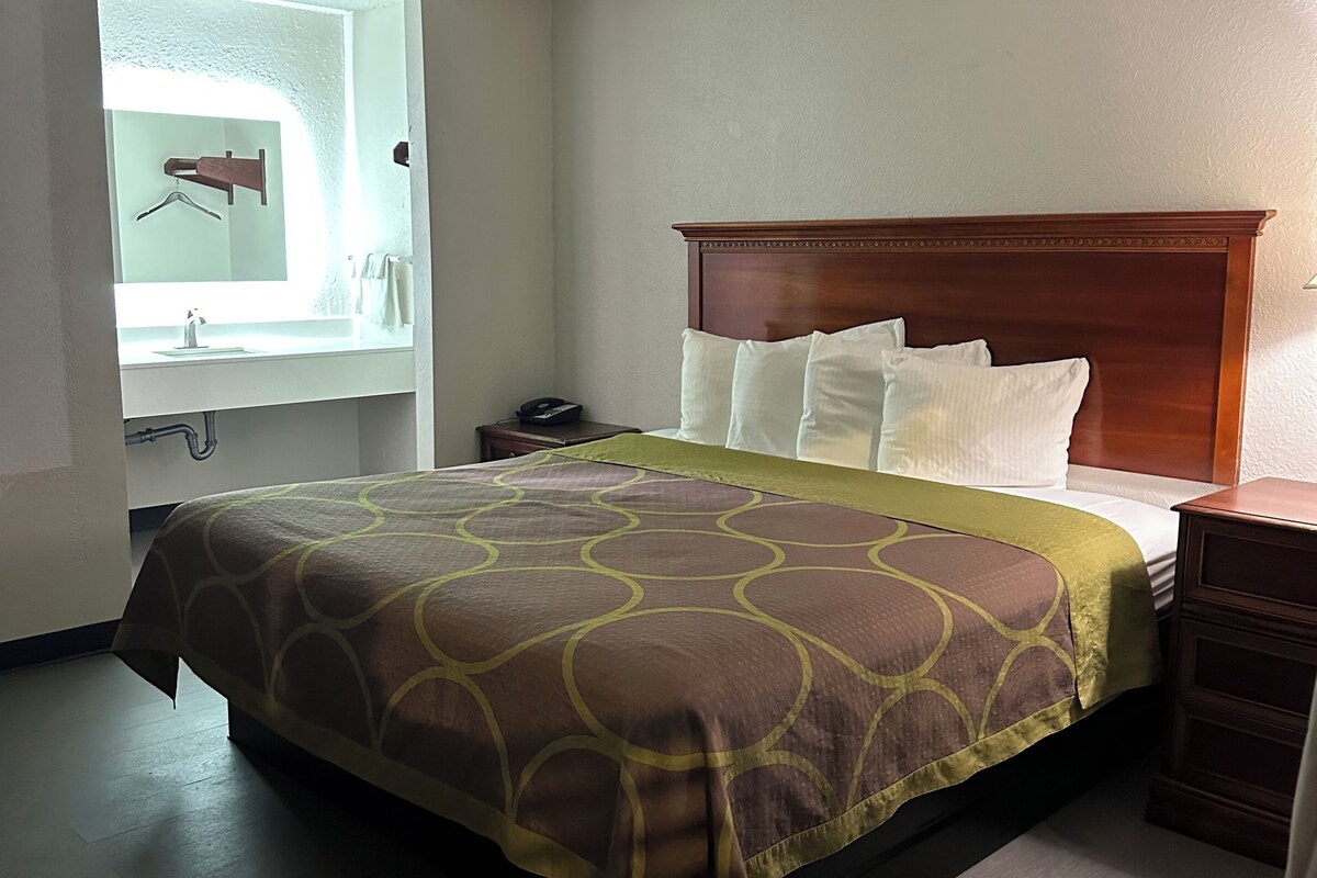 Une chambre d’hôtel comprenant un lit, une table de chevet, une commode, un miroir et une salle de bain avec un porte-serviettes.