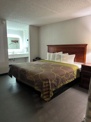 Une chambre d’hôtel comprenant un lit, une table de chevet, une commode, un miroir et une salle de bain avec un porte-serviettes.