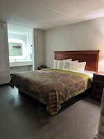 Una habitación de hotel con cama, mesita de noche, cómoda, espejo y baño con toallero.