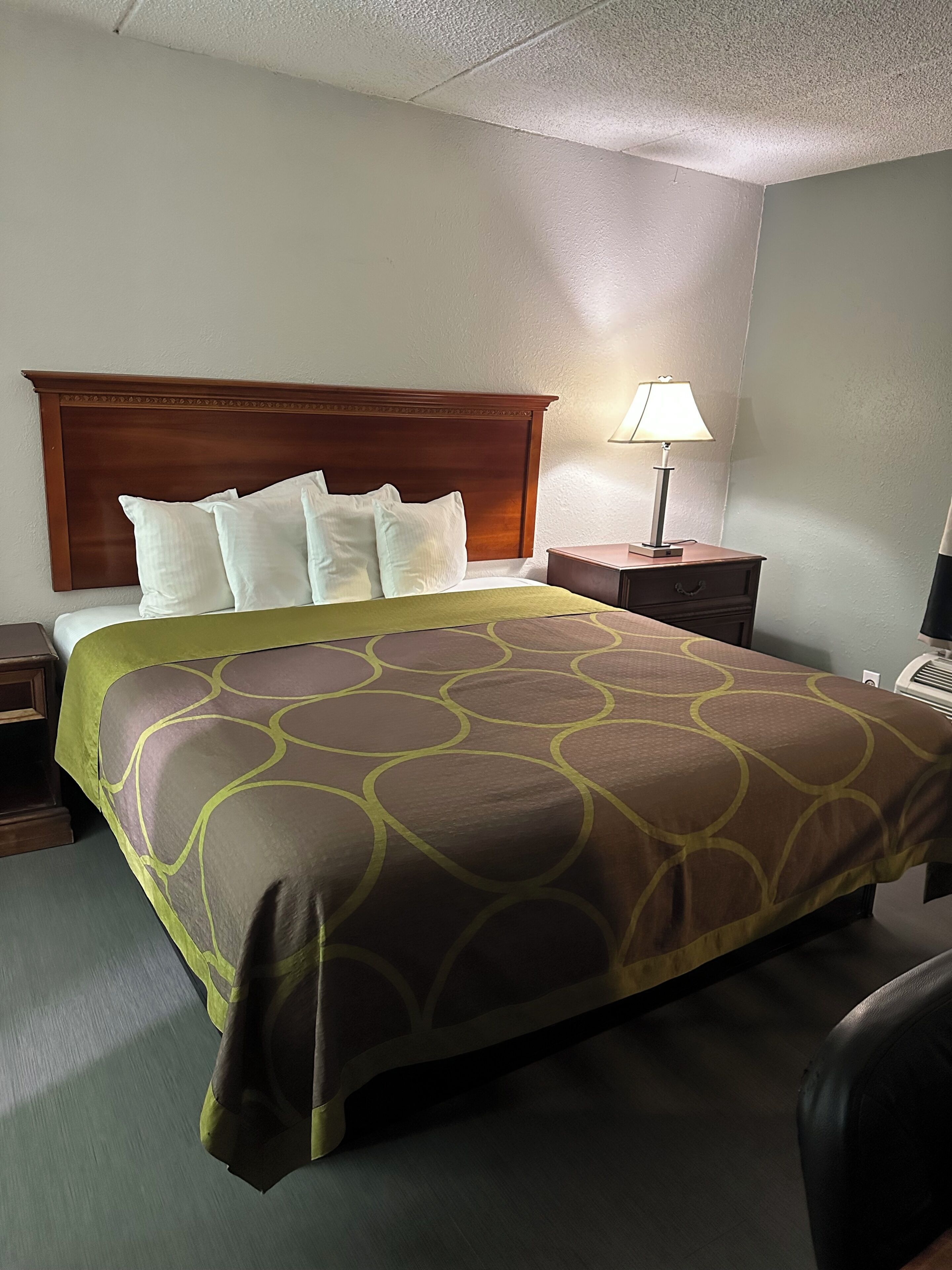A hotel room with a bed, a nightstand, a lamp, and a chair.