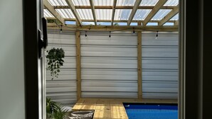 Eine Holzterrasse mit Pool, einer Pergola mit Lichterketten und einem Topfpflanzen.