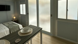 Ein Zimmer mit einem Bett, einem Tisch mit Schüssel und Hut, einem Fernseher und einem Fenster mit Milchglas.