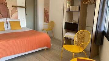 A hotel room with a bed, a yellow chair, a small table, a wardrobe, and a mirror.