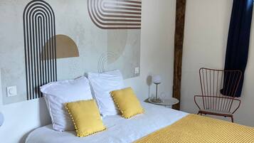 Un dormitorio moderno con una cama grande, ropa de cama blanca y amarilla, un cuadro abstracto geométrico, una pared de acento de madera y una silla roja.