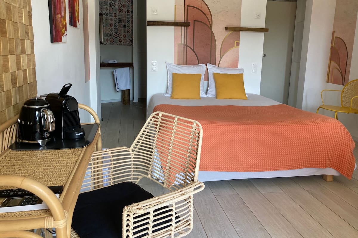 A hotel room with a bed, a chair, a table with a coffee maker, and a wall with artwork.
