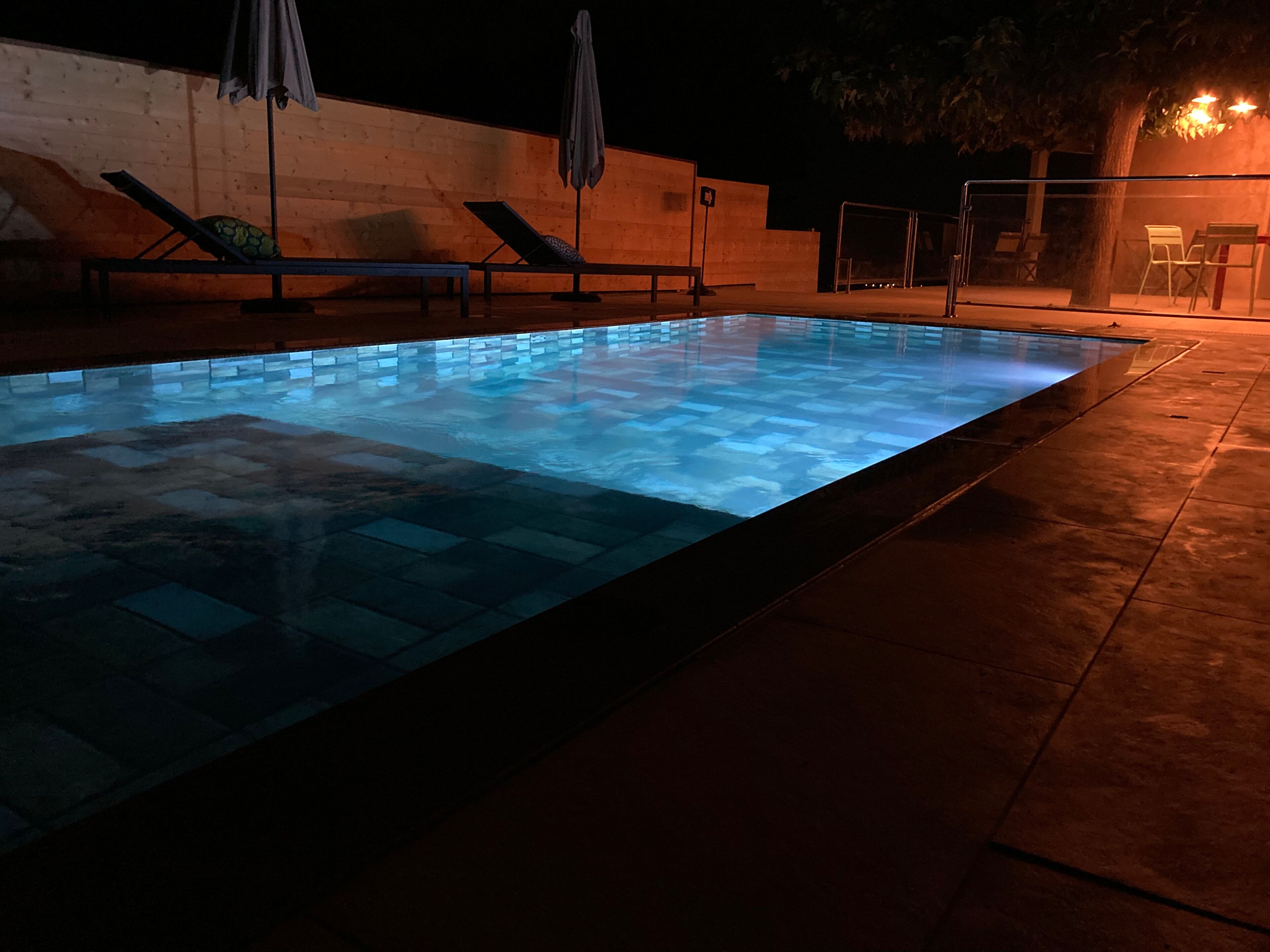 A swimming pool with lounge chairs and umbrellas, surrounded by a tiled deck.