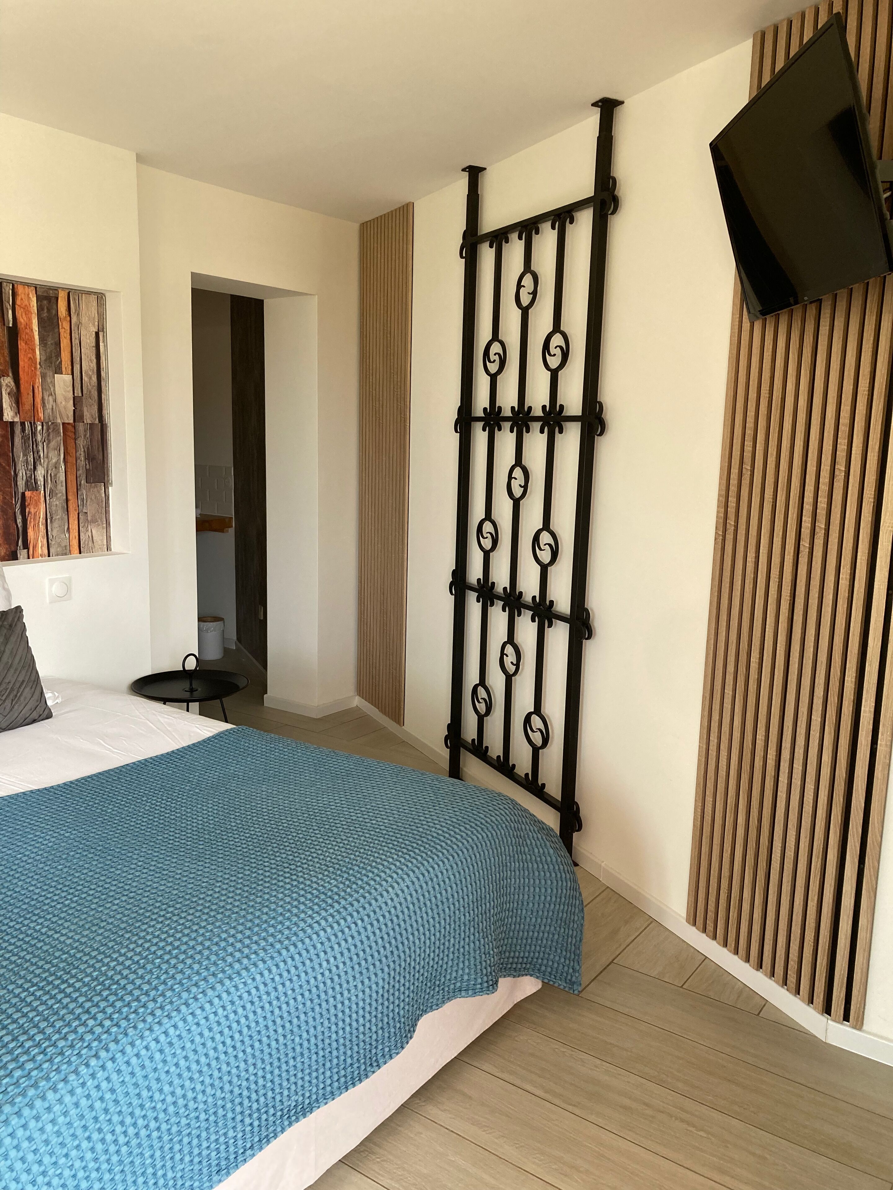 A bedroom with a bed, a wall-mounted TV, a decorative metal partition, and a wooden panel on the wall.