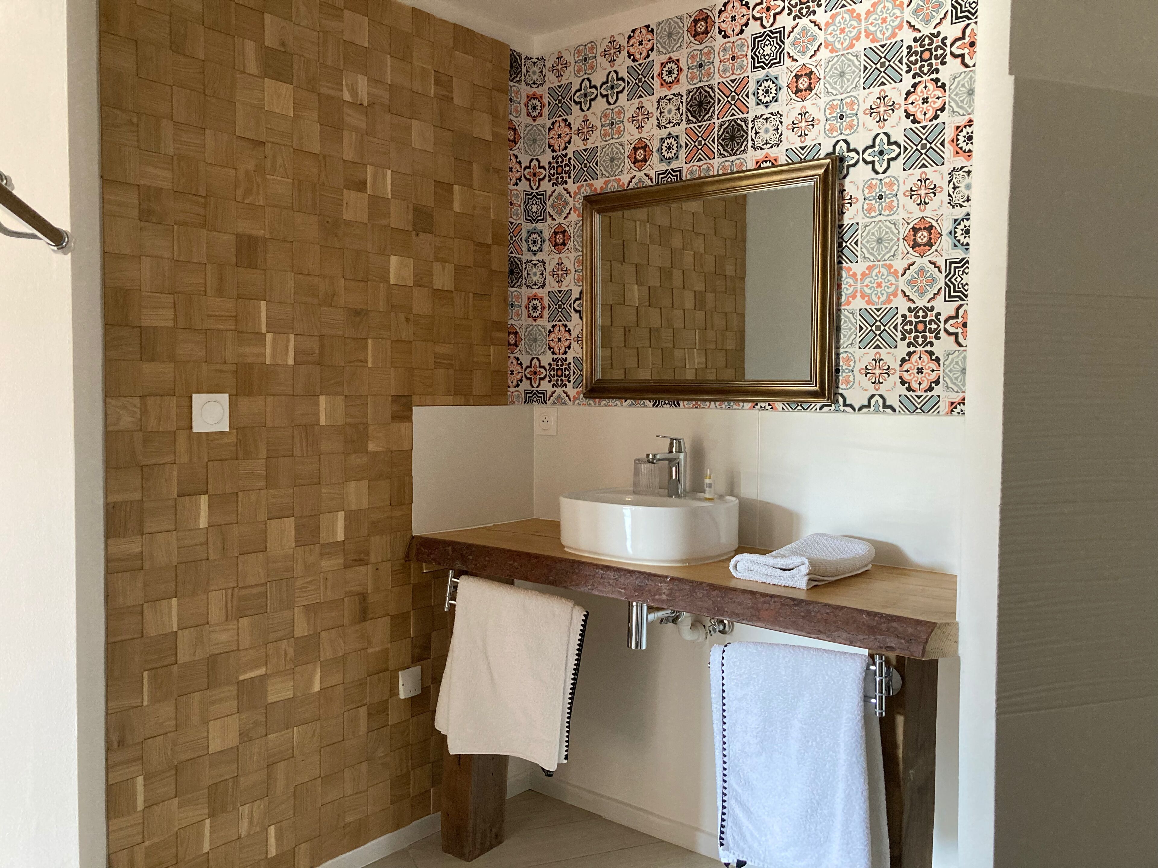Ein Badezimmer mit Holzwand, gefliestem Fliesenspiegel, Waschbecken in Weiß, einem Spiegel und zwei Handtüchern.