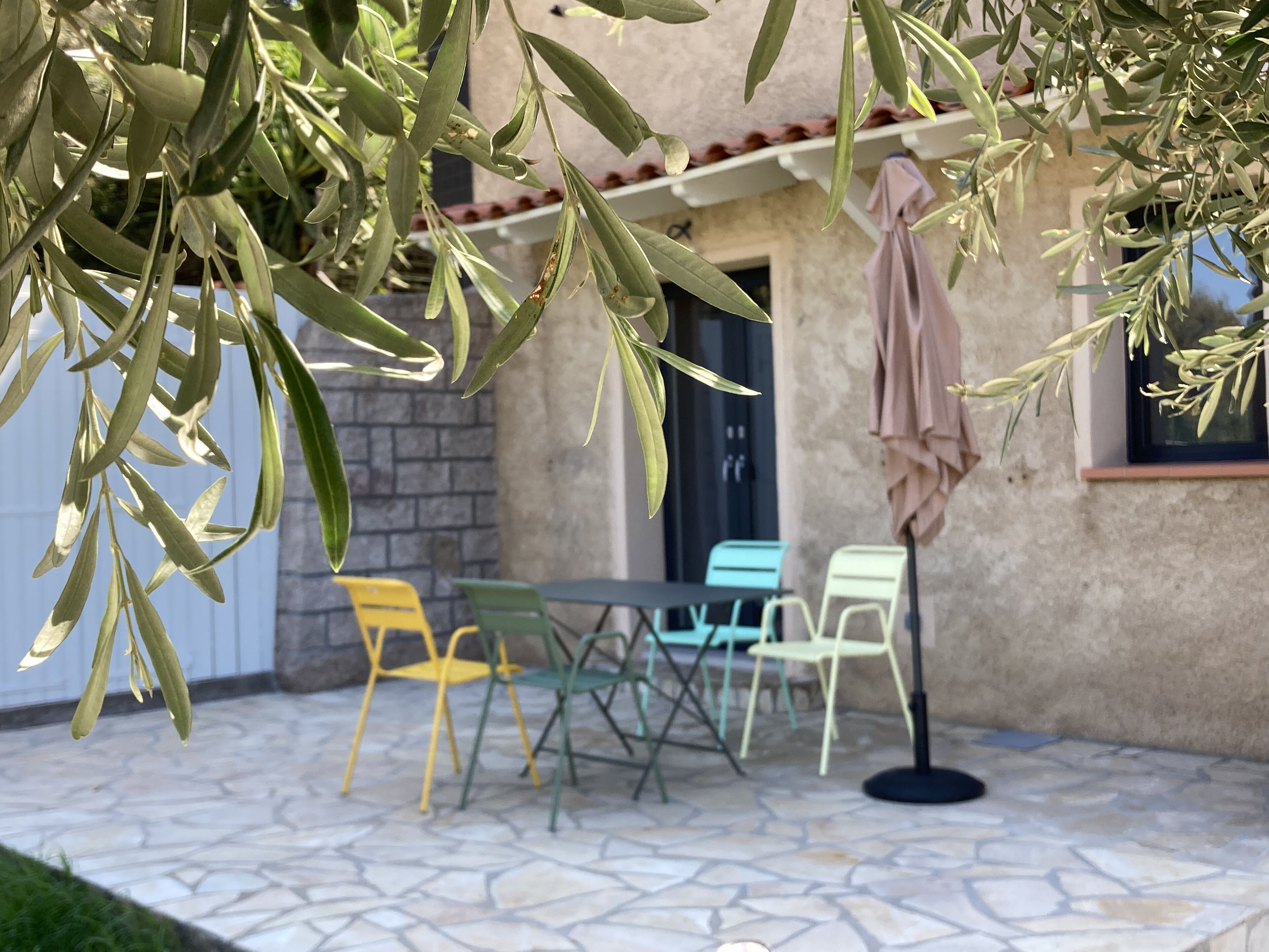 An outdoor patio with a stone floor, a table with chairs, and a hanging umbrella.