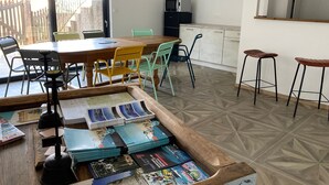 A dining area with a wooden table, chairs, and a tray of magazines. There is a kitchen area with cabinets and a microwave.