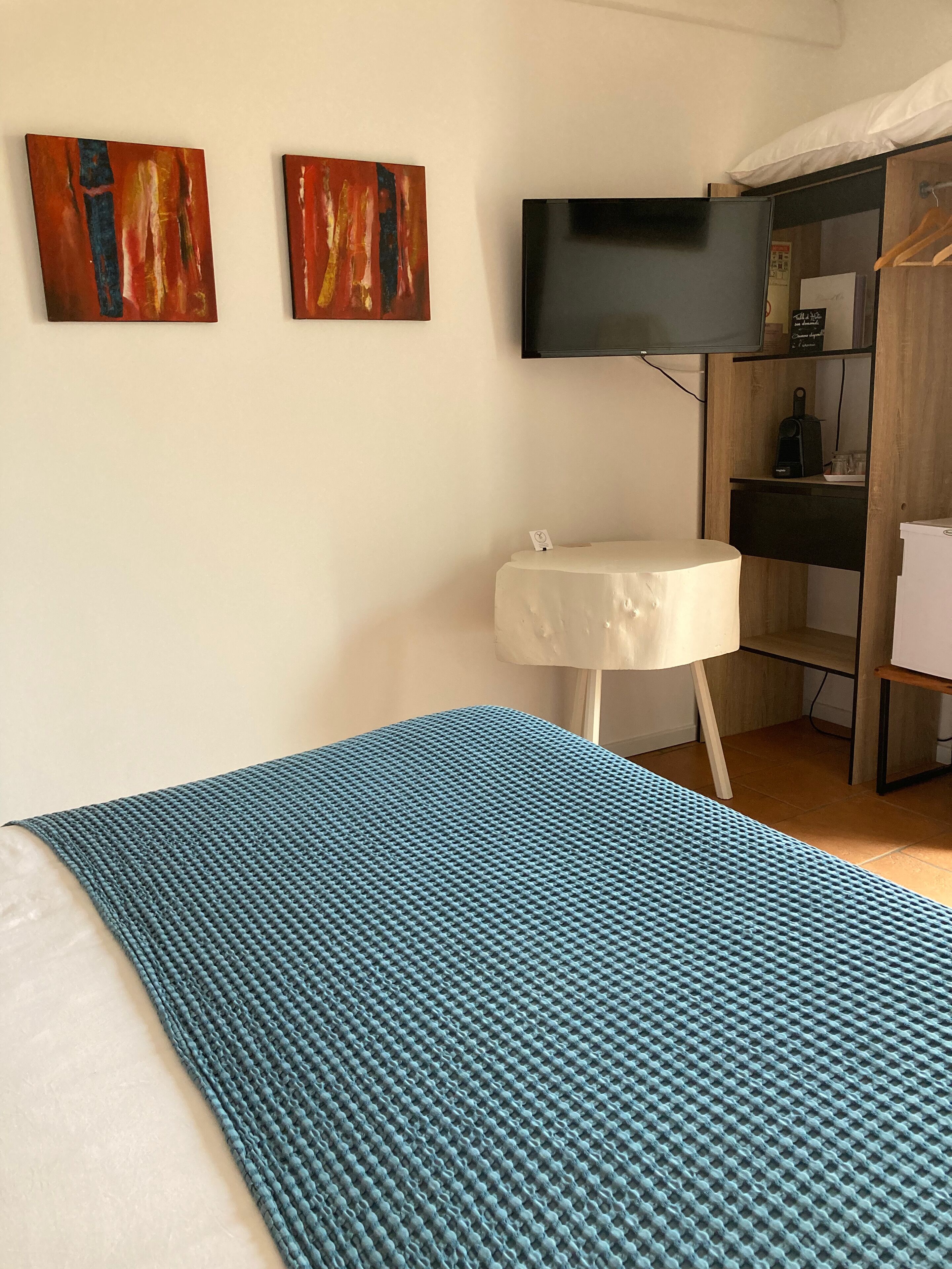 Une chambre d’hôtel avec un lit, une petite table, un téléviseur fixé au mur et deux tableaux abstraits.