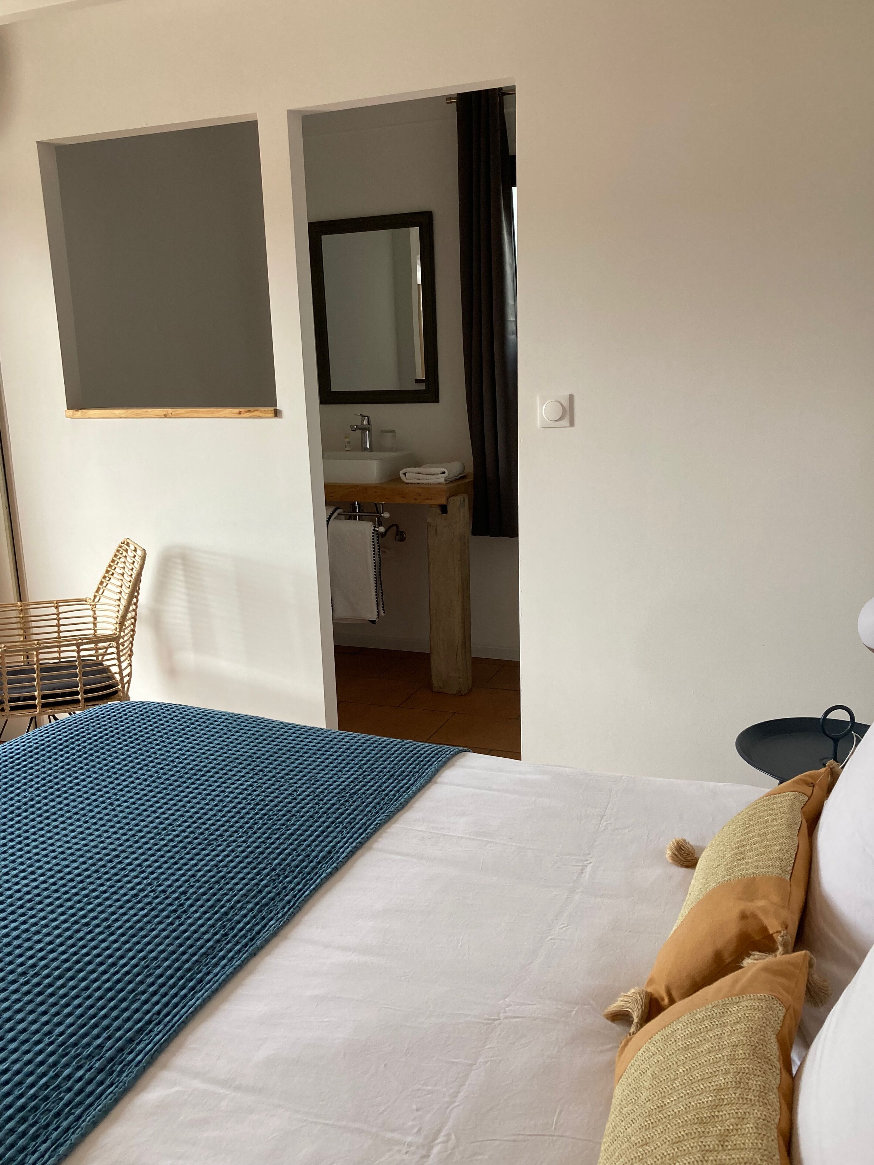 A bedroom with a bed, a bedside table, a chair, and a view into the bathroom.