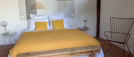 Un dormitorio con una cama de madera, ropa de cama blanca y amarilla, una silla roja y una obra de arte abstracta moderna en la pared.