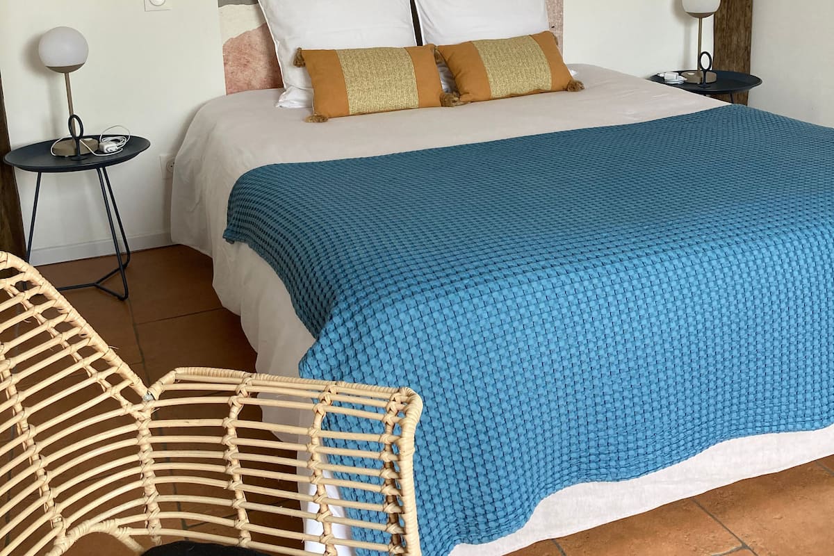 A bedroom with a bed, two bedside tables, a woven chair, and a textured wall.