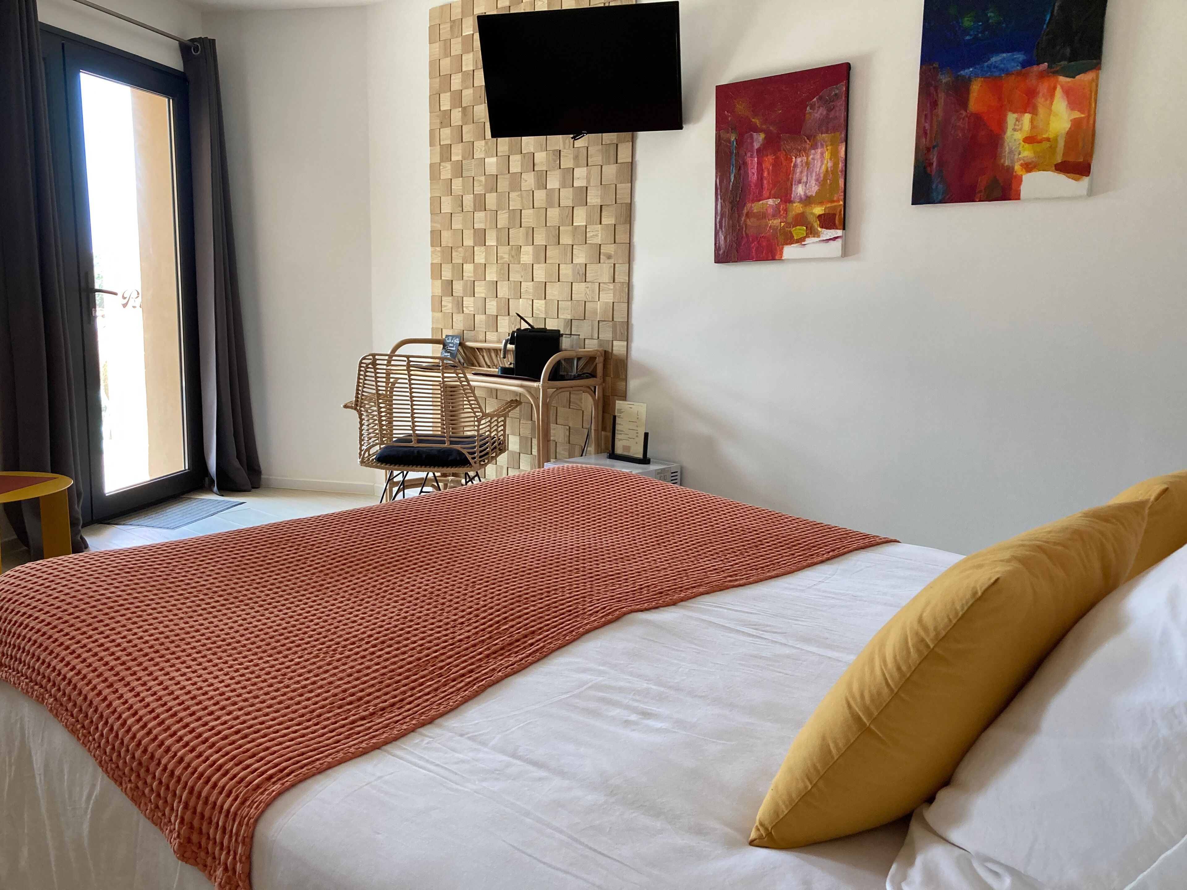 Een hotelkamer met een bed, een televisie aan een houten wand bevestigd, een stoel en een tafel.