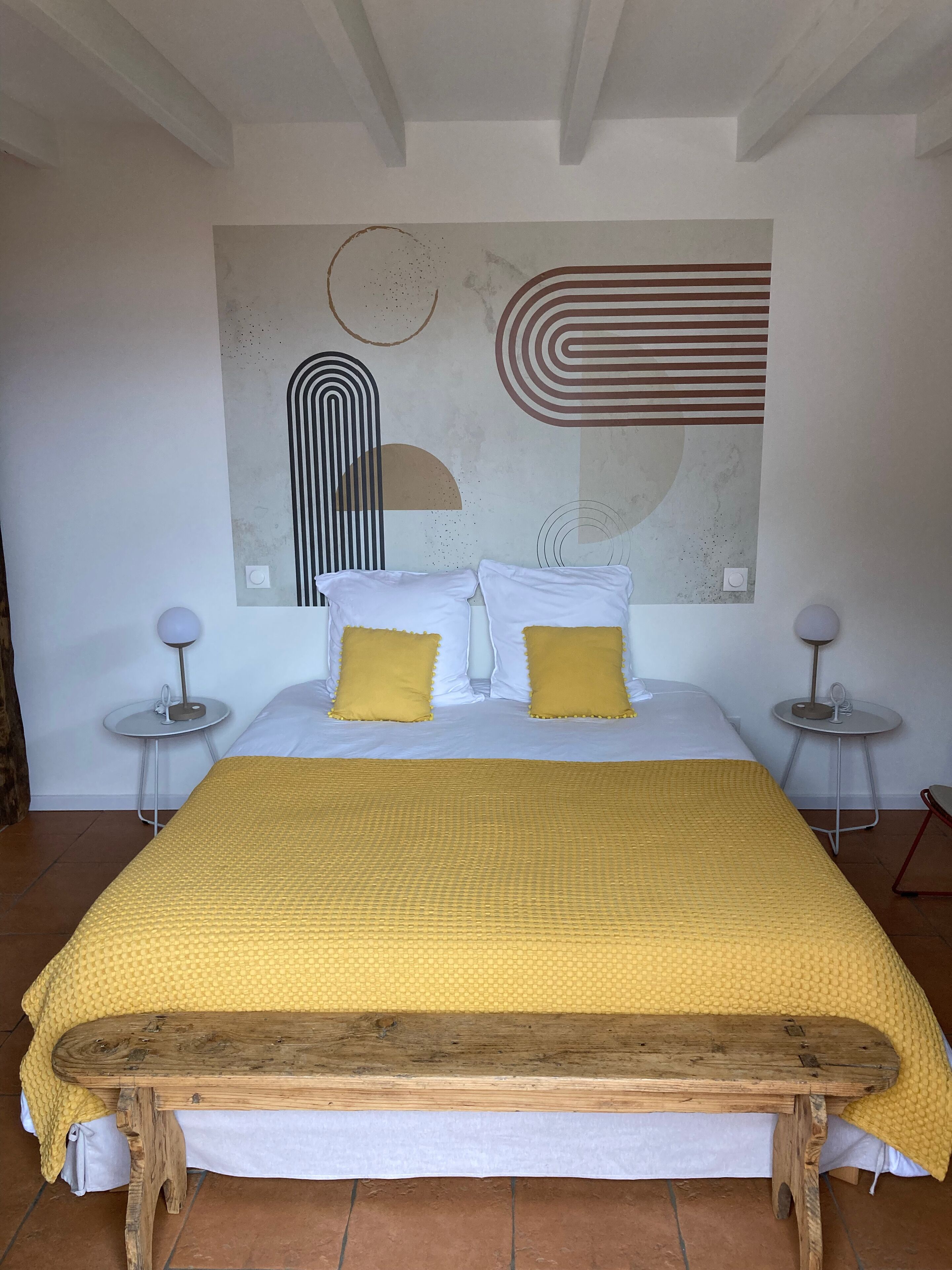 A bedroom with a large bed, two bedside tables, a wooden bench, and abstract wall art.