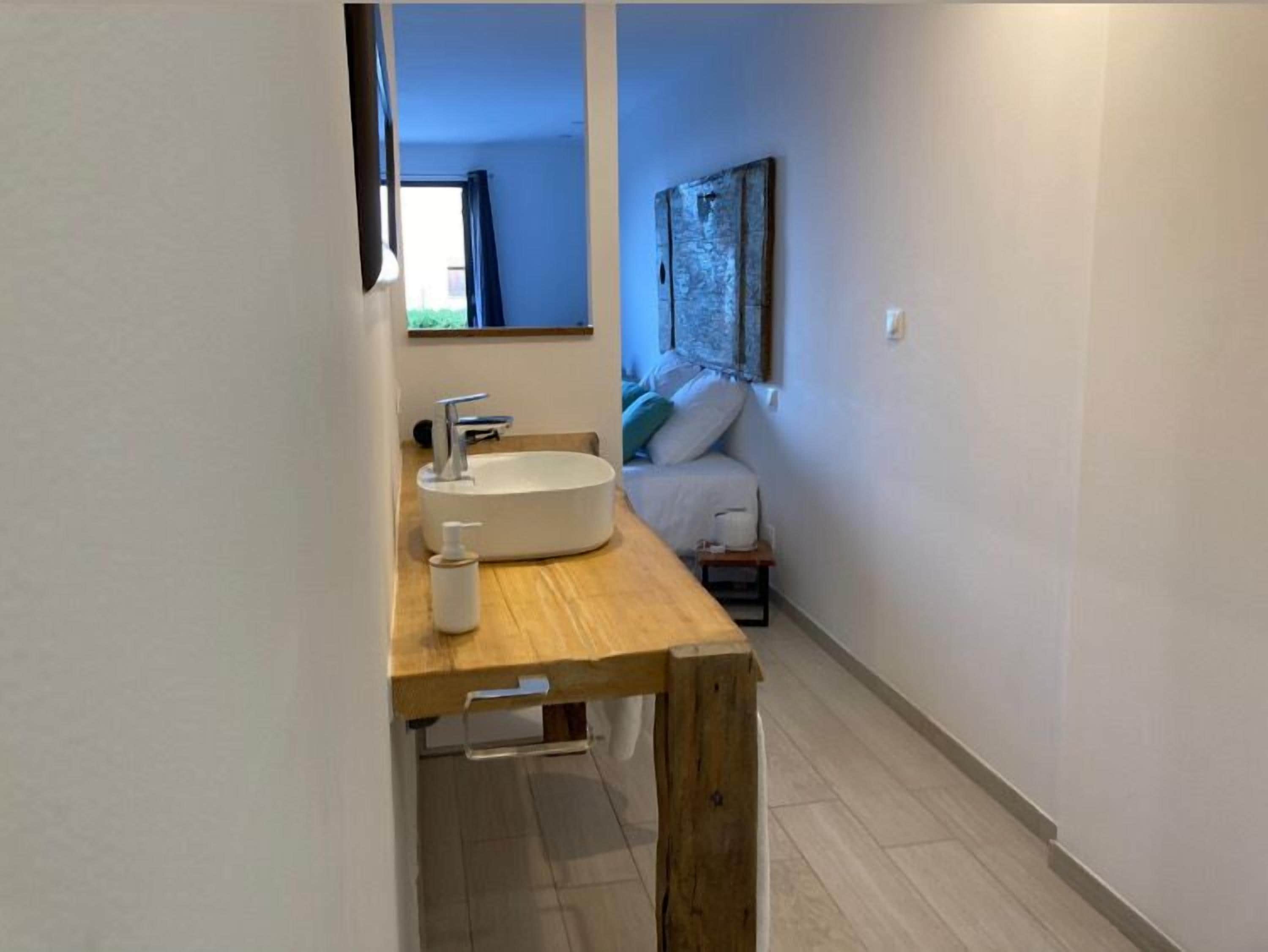 A modern bathroom with a wooden vanity, a round sink, and a small bedside table.