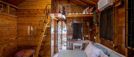 A wooden cabin with a loft bedroom, a desk, and a small bench.