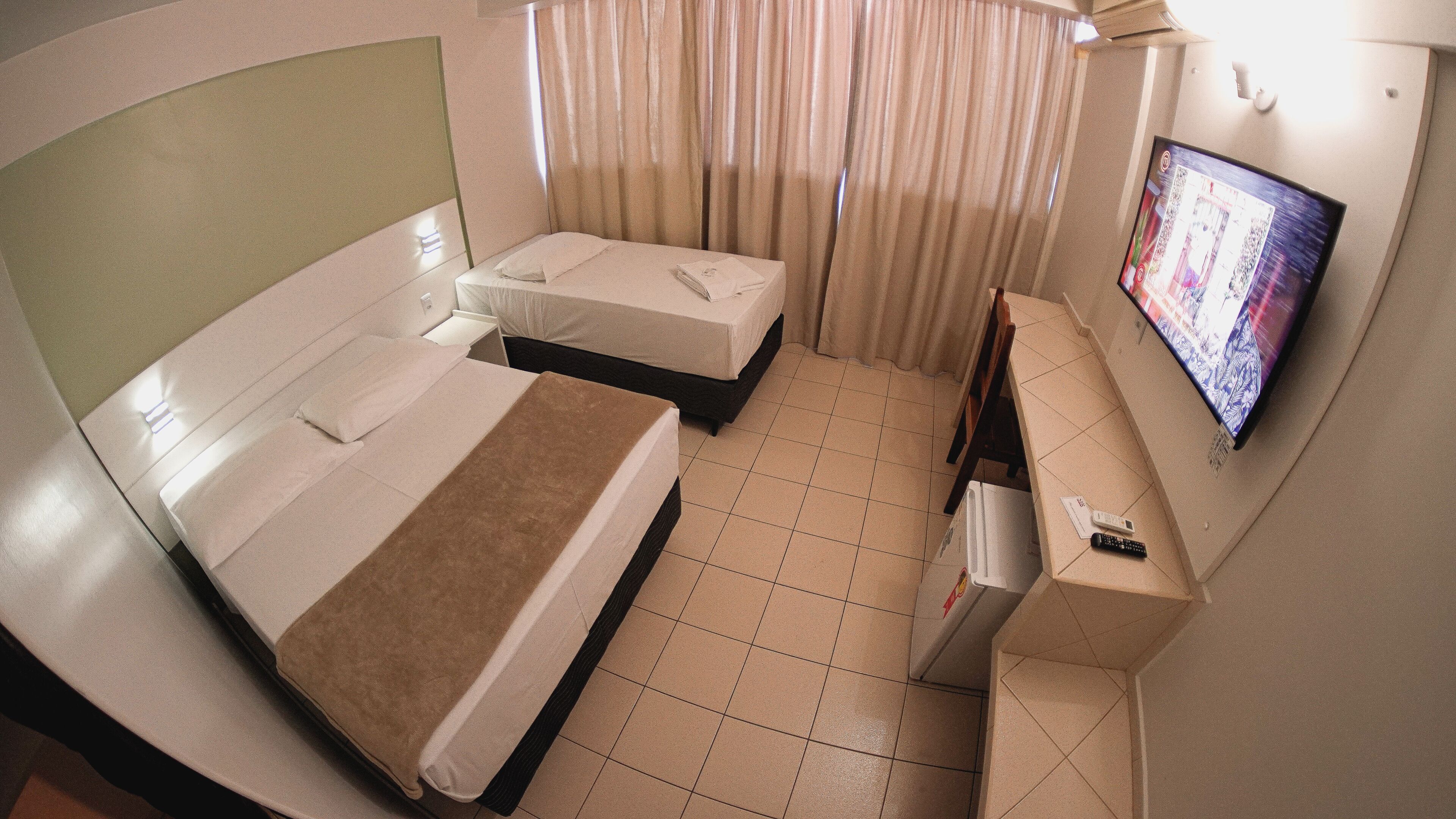 Quarto de hotel com duas camas, televisão e pequena escrivaninha com controle remoto.